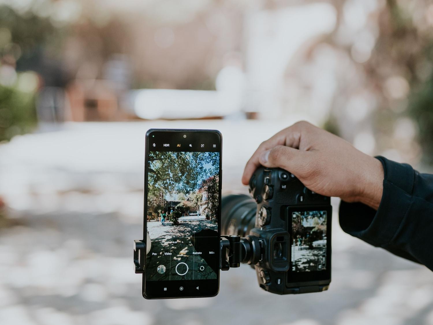 Smartphone and DSLR camera held side by side comparing mobile phone and professional camera photography.